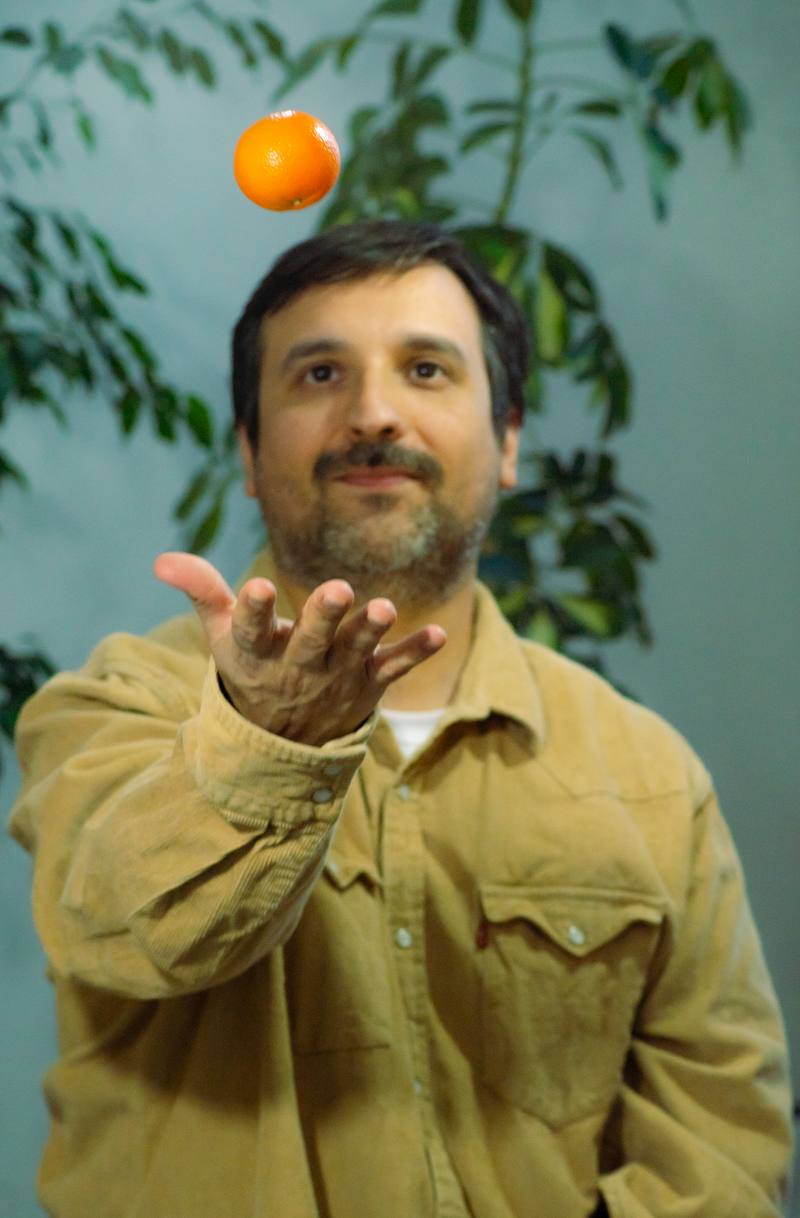 Joaquín lanza una naranja al aire con la mano abierta, frente a una planta