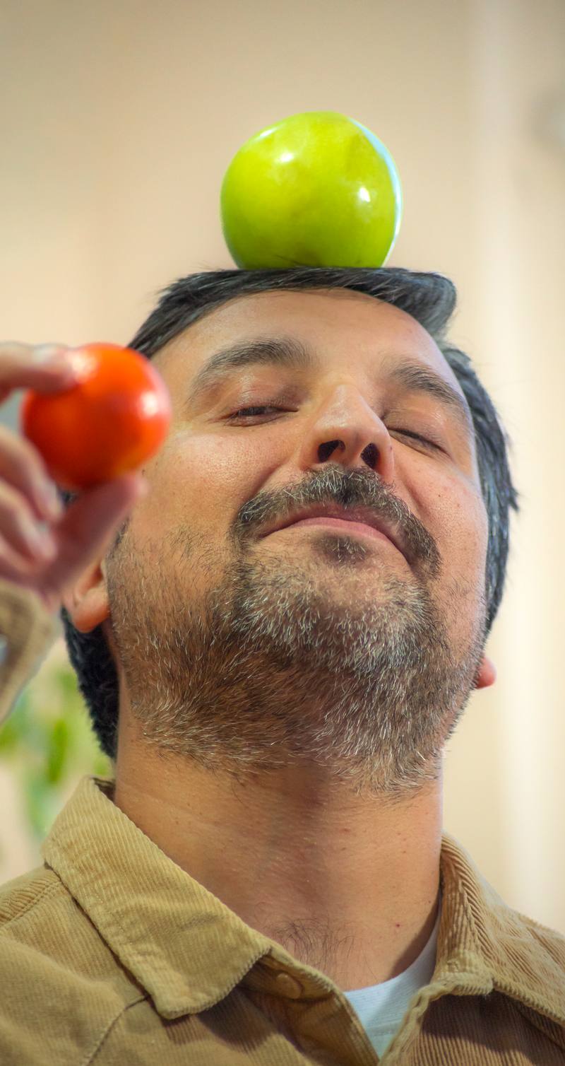 Joaquín con los ojos cerrados, una manzana en la cabeza y una naranja en la mano